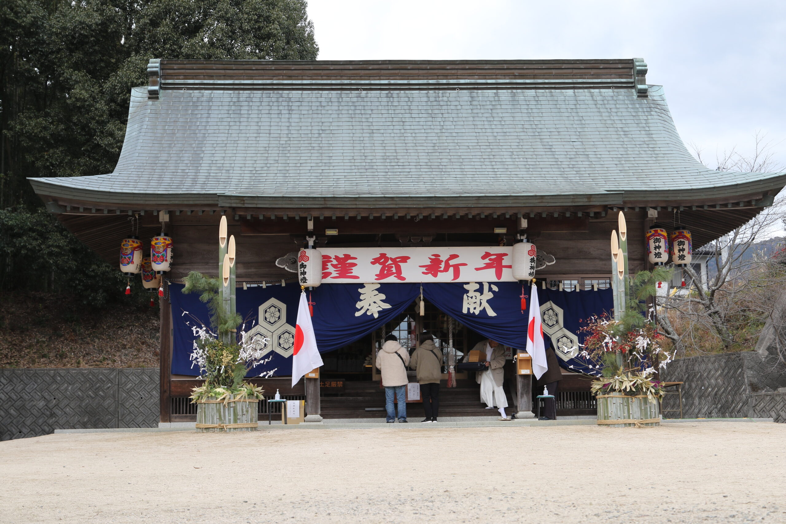 Stone torii gate at a small Japanese Shinto shrine decorated for the New Year, with stone steps leading upward and colorful banners hanging above.